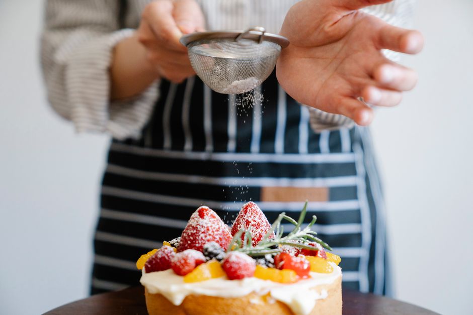 Close-up of a chef sprinkling powdered sugar on a fruit tart with strawberries, perfect for dessert indulgence.